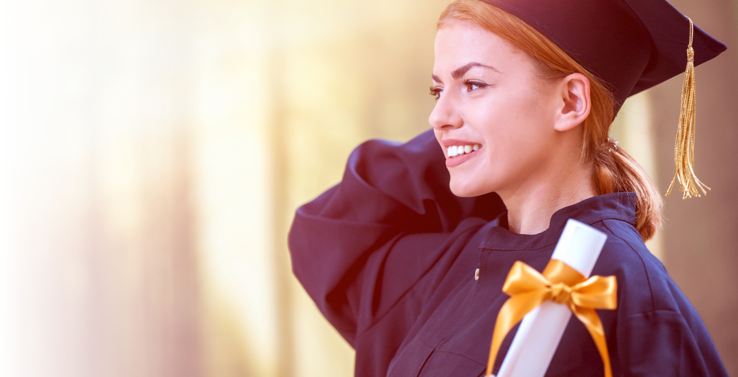 Foto de moa com toga de formatura e barrete segurando um diploma com lao dourado.e olhando para o horizonte.